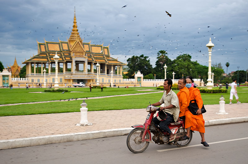 Monks ride on the back of a motorbike as it drives past the Chan Chaya pavilion in central Phnom Penh